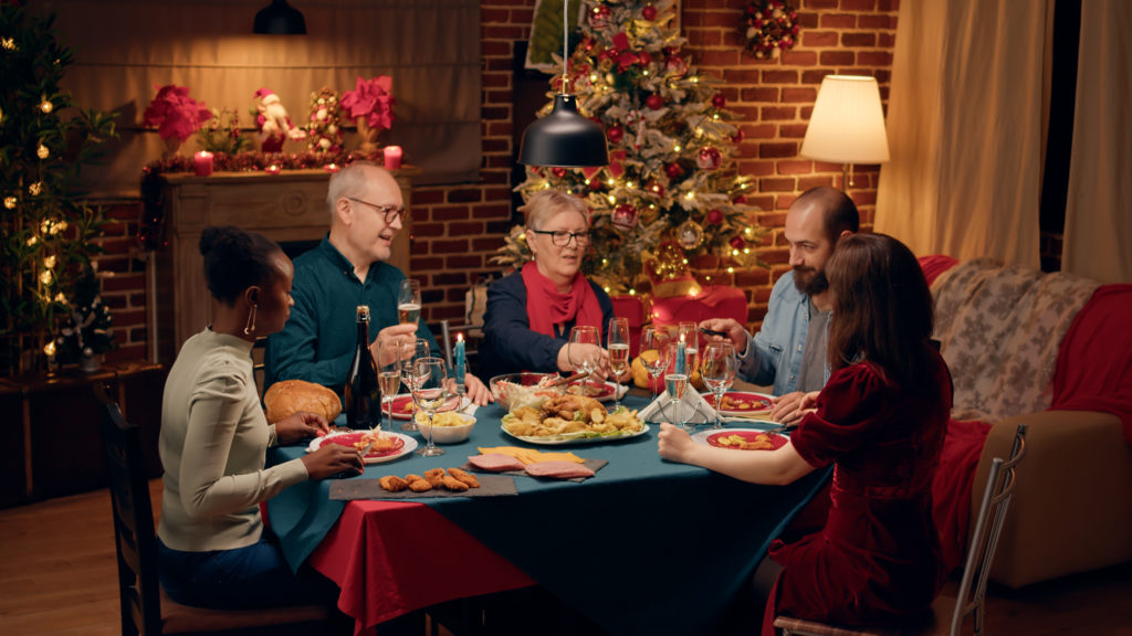 Laughing Diverse People Gathered Around Christmas Dinner Table Clinking Wine Glasses Happy Smiling Heartily Family Members Celebrating Traditional Winter Holiday Home 1024x576
