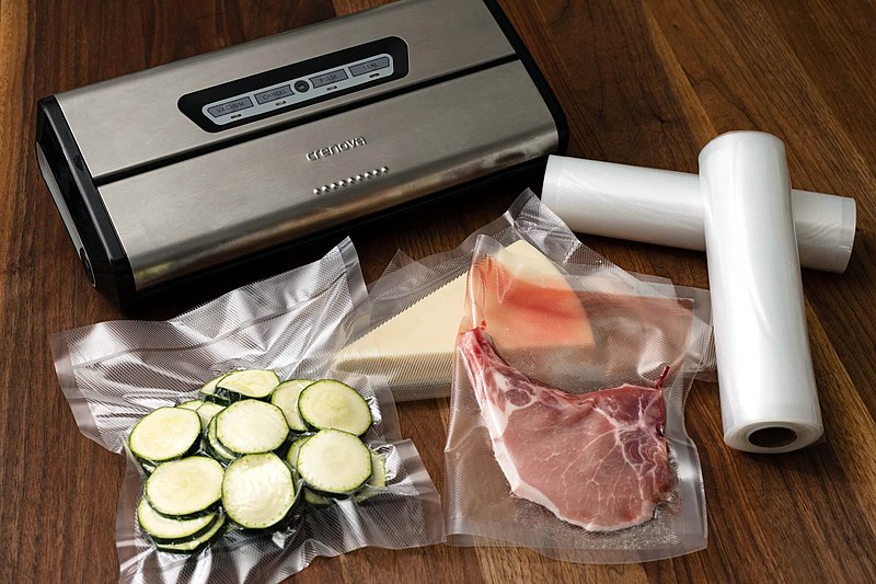 800px Vacuum Sealer With Food Sealed On Wooden Table And Rolls Of Plastic For Sealing
